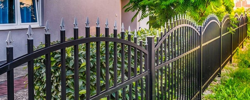 Reja de herrería abatible con disño de barras con punta de lanza en un jardín