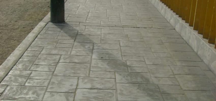 Banqueta con diseño de concreto estampado al lado de casas y avenida en remodelación